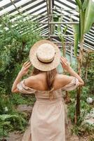 A beautiful young woman takes care of plants in a greenhouse. The view from the back. Concept of gardening and an eco-friendly lifestyle. photo