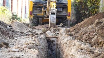 Excavator digs a trench to lay pipes. Close up of an excavator digging a deep trench. An excavator digs a trench in the countryside to lay a water pipe. Slow motion video