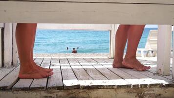Two woman in the changing, dressing room on beach, at sunset on the seashore. Close-up of bare female feet legs in enclosed changing room cabin. Summer holiday vacation and travel concept. Slow motion video