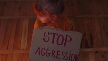 Afraid homeless toddler girl sitting holding inscription Stop Aggression, hiding from bombing attack video