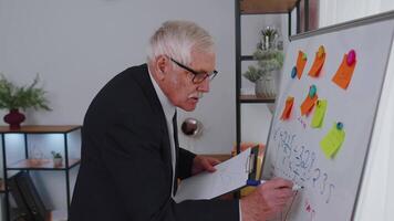 Senior business man making notes on board with stickers analyzing infographics use laptop computer video