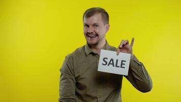 contento uomo mostrando vendita parola iscrizione, sorridente, guardare soddisfatto con Basso prezzi. lento movimento video