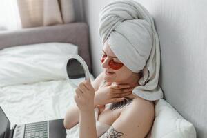 Tver, Russia-august 2, 2021 A woman after a shower is lying on the couch with a laptop and an eye mask at the same time. The concept of multitasking in the twenty-first century. photo