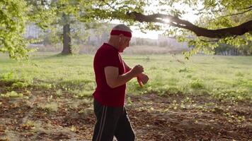 Male senior person running along the road in park. Mature runner man training, listening music video