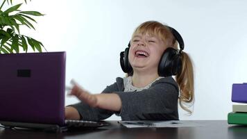 Child schoolgirl kid laughing and smiling. Learning lessons at home and using laptop computer video