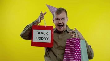 Smiling man showing Black Friday inscription on shopping bags, celebrating, rejoicing good discounts video