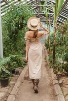 A beautiful young woman takes care of plants in a greenhouse. The view from the back. Concept of gardening and an eco-friendly lifestyle. photo