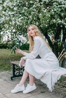 A blonde girl with long hair on a walk in a spring park. Springtime and blooming apple trees. photo