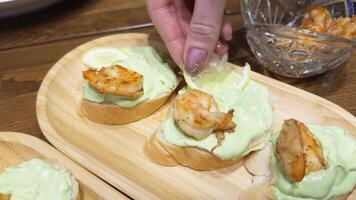 A woman's hand decorates sandwiches with avocado and shrimp on the dinner table by adding lemon slices. video