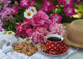 Beautiful still life with peony flowers, vintage cup and cookies on the table. Romantic greeting card for birthday, Valentines, Mothers Day concept. Summer background with vintage objects photo