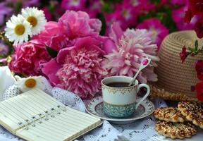 Beautiful still life with peony flowers, vintage cup and cookies on the table. Romantic greeting card for birthday, Valentines, Mothers Day concept. Summer background with vintage objects photo