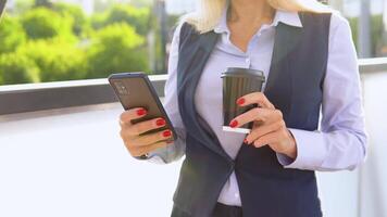 donna d'affari in piedi al di fuori un' moderno aziendale edificio con caffè tazza e cellulare. paesaggio urbano sfondo video