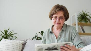 Senior woman with glasses reads newspaper at home video