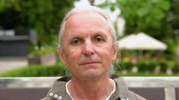 portrait de personnes âgées homme sourire à vous Extérieur. élégant personnes âgées homme avec longue cheveux souriant sur banc dans Publique ville parc video