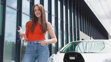 A girl stands with charger near her electric car video