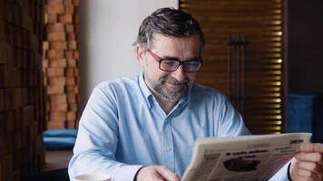 Senior man reads a newspaper sitting in a cozy cafe video