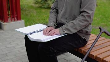 Sénior aveugle homme séance sur banc dans ville parc et en train de lire une braille livre video