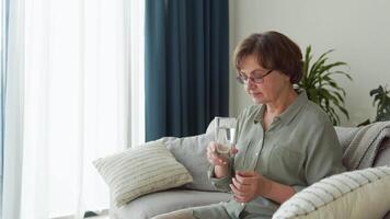 Beautiful old lady drinking water sitting on the sofa at home video