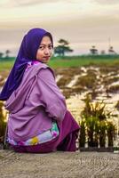 Rear view of a Muslim woman sitting in a rice field after harvesting with her head facing the camera. photo