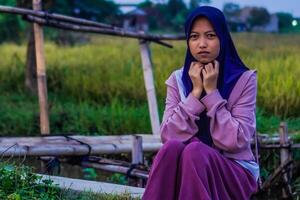 Muslim woman is sitting on the edge of a rice field with her hands together. rice fields background with copy space. photo