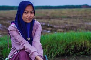 musulmán mujer es sentado en el borde de un arroz campo con su manos juntos. arroz campos antecedentes con Copiar espacio. foto