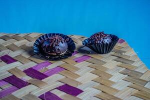 Isolated chocolate dumplings, close-up view of chocolate dumplings sprinkled with sprinkles, with woven bamboo as a base and ornamental plants on the side. Eid meal concept. photo