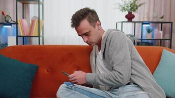 Man sitting on couch using credit bank card and smartphone while transferring money online shopping video