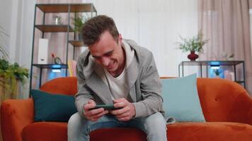 Worried funny young man boy playing shooter online games celebrate win on smartphone at home video