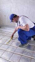 hombre trabajador toma mediciones durante el instalación de un calentar piso. calentar piso calefacción sistema. video