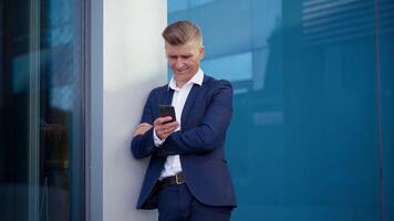 ein Mann im ein passen gelehnt gegen ein Gebäude während suchen beim seine Telefon video