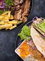 Beef brisket with potato and green salad and tacos server on plate over black background. top view flat lay photo