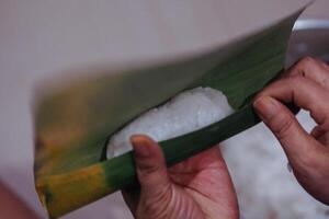 closeup of hands making lontong wrapped in banana leaves photo