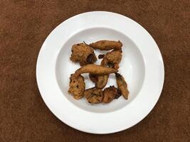 Mirchi pakora or Mirchi bhajji served in a white plate, a famous midday snack in india, served over a rustic wooden background, selective focus photo