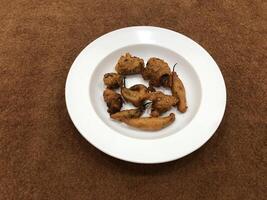 Mirchi pakora or Mirchi bhajji served in a white plate, a famous midday snack in india, served over a rustic wooden background, selective focus photo