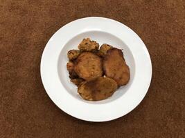 Mirchi pakora or Mirchi bhajji served in a white plate, a famous midday snack in india, served over a rustic wooden background, selective focus photo