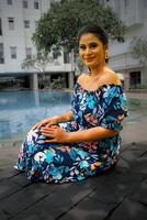 tangerang, Indonesia - 9 9 diciembre 2023 un hembra modelo en un sentado pose, levantamiento su Derecha mano y participación su largo cabello, vistiendo un floral estampado vestido, sonriente a el cámara foto