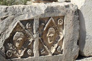 Historical stone bas-relief with carved faces in ancient city of Myra on sunny day. Dead civilization. Ruins of rock tombs in Lycia region, Demre, Antalya, Turkiye photo