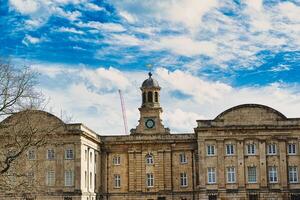 Historic stone building with a central clock tower under a blue sky with fluffy clouds, featuring classic architecture and a construction crane in the background in York, North Yorkshire, England. photo