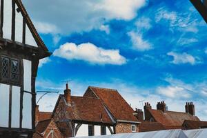 Quaint European village with traditional half-timbered houses and terracotta rooftops under a vibrant blue sky with fluffy clouds in York, North Yorkshire, England. photo