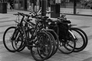 Black and white image of multiple bicycles locked to a bike rack in an urban setting, with a blurred background of a city street photo