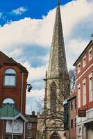 ancient church spire reaching into a blue sky with clouds, flanked by traditional brick buildings, showcasing architectural contrast and historical cityscape in York, North Yorkshire, England. photo