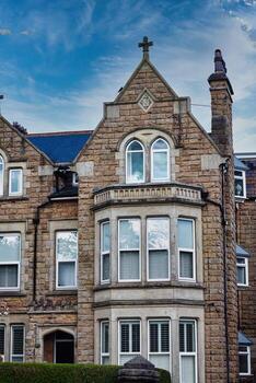 Victorian-style stone building with a gabled roof and bay windows under a blue sky with clouds, showcasing classic architectural details and craftsmanship in Harrogate, North Yorkshire. photo