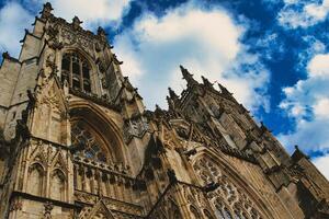 Gothic cathedral's facade with intricate stone carvings against a vivid blue sky with fluffy clouds, showcasing architectural grandeur and historical elegance in York, North Yorkshire, England. photo