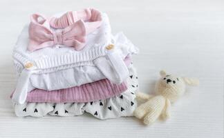 Stack of baby clothes, pink headband and knitted toy bunny. photo