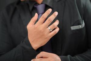 Wedding ring photo shoot concept a man wearing a formal black suit and purple tie is holding a wedding ring