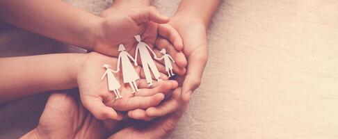 Adult and children hands holding paper family cutout, family home, foster care, homeless support concept photo