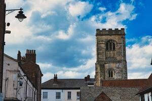 Quaint European street with historic buildings and a prominent church tower under a dramatic sky with fluffy clouds in York, North Yorkshire, England. photo