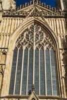 Gothic architecture detail of a cathedral window with intricate tracery and stained glass, set against a clear blue sky in York, North Yorkshire, England. photo