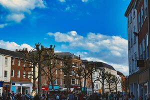 Bustling city street scene with pedestrians, unique pruned trees under a blue sky with clouds, and historic buildings, capturing the essence of urban life in York, North Yorkshire, England. photo