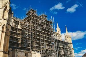 Historic cathedral undergoing renovation, with intricate scaffolding against a bright blue sky with clouds. Architectural preservation concept in York, North Yorkshire, England. photo